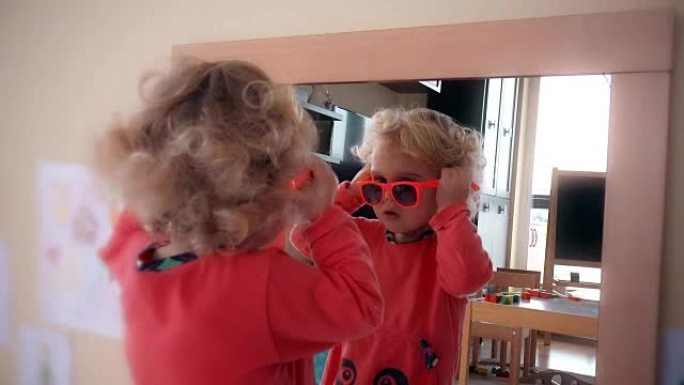 可爱的小女孩把红色太阳镜戴在镜子附近的头上