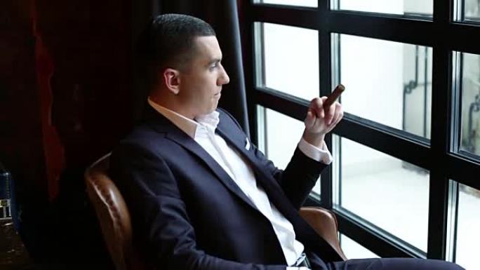 男人要抽烟了。穿着经典西装的年轻商人坐在窗前。