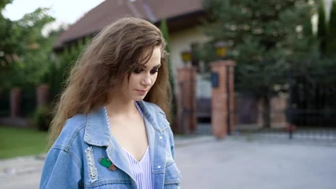在一个温暖的夏日里，一个穿着鲜艳的妆扮和长长的卷发的年轻女子走在街上