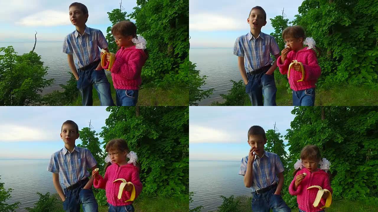孩子们在一个大湖岸边的森林里休息。女童吃香蕉。少年少年讲述他的故事。