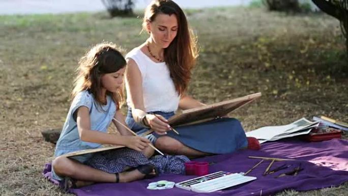 年轻女子在阳光明媚的夏日在公园教画一个女孩。