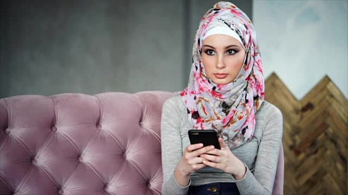 美丽的穆斯林妇女，戴着鲜艳的头巾，坐在粉红色的沙发上