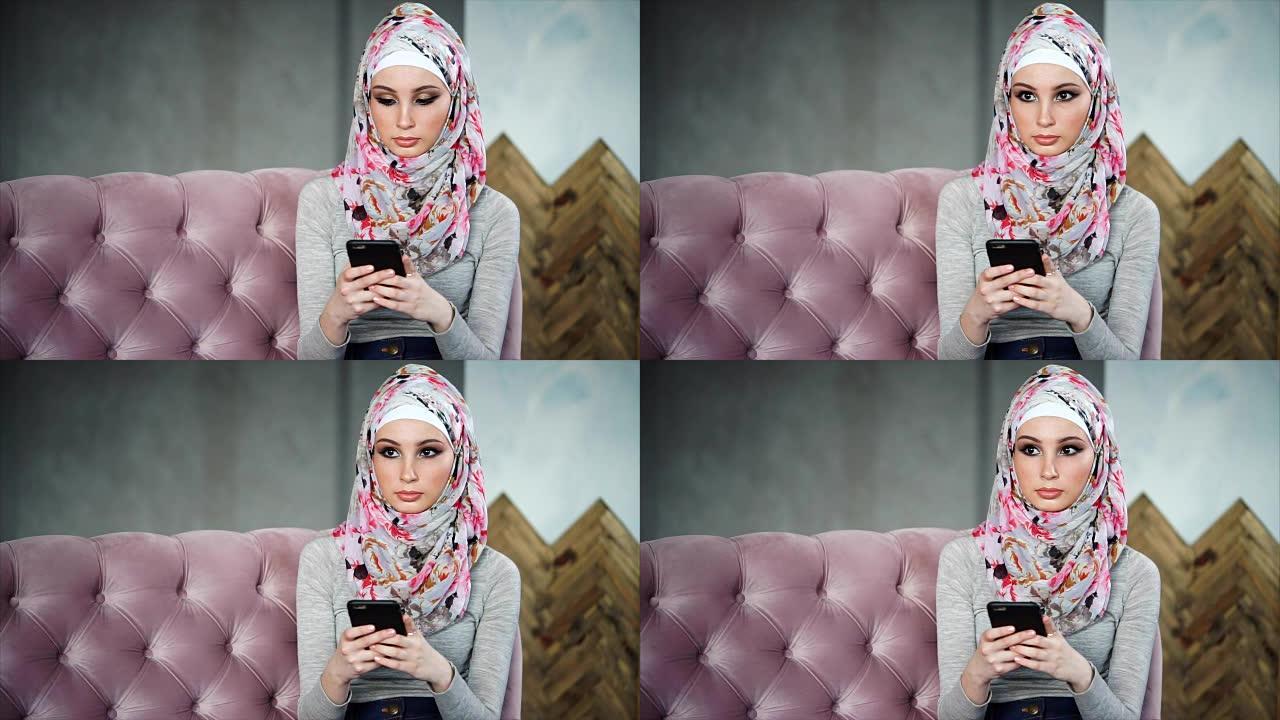 美丽的穆斯林妇女，戴着鲜艳的头巾，坐在粉红色的沙发上
