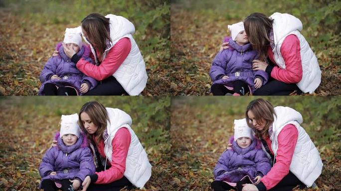 秋天公园里哭泣的小女孩。母亲安慰一个哭泣的孩子。脸颊上的泪水