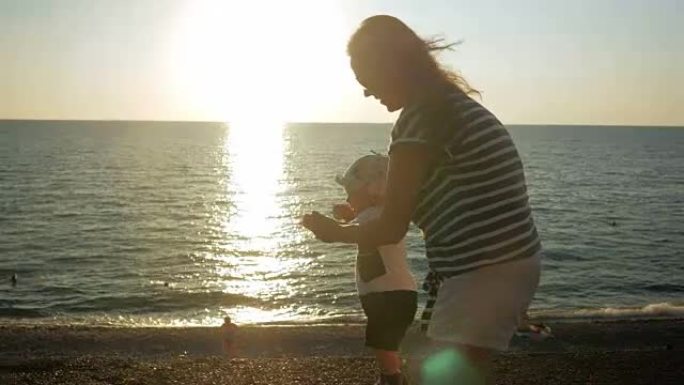 日落时，年轻的母亲和可爱的婴儿在海滨散步。婴儿仍然很穷，我妈妈经营着它。人生第一步的概念