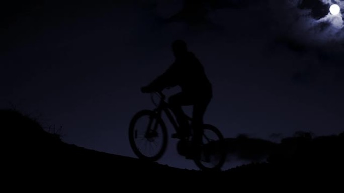 星空背景下夜间在山上出现的骑自行车者的剪影
