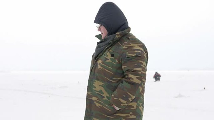 这个人从事冬季捕鱼。它的费用是等待鱼竿的费用。穿着防护服暖和