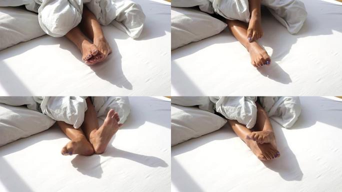 在一个阳光明媚的早晨，被拉扯毯子的女人在床上赤脚的特写镜头