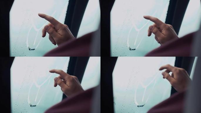 一名男子用一根手指在车内窗户上画画。外面有雨的天气。滴