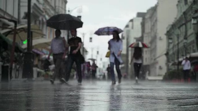 城市街道雨天的背景。实时。雨中带伞的人上下班。拿着五颜六色雨伞的年轻女孩。模糊的波克。自然背景