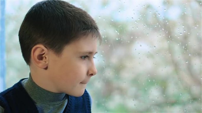 悲伤的男孩坐在窗边，雨滴