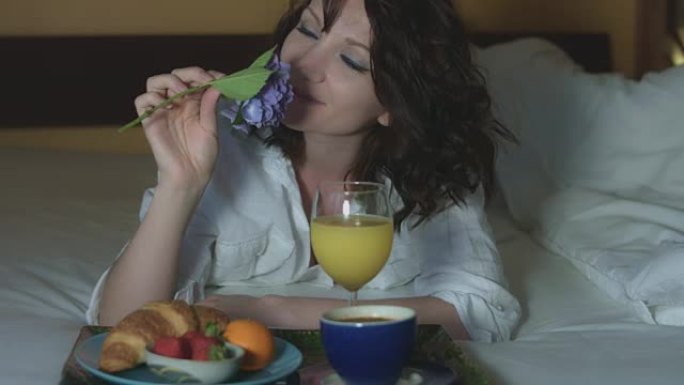 一个性感女人闻着花和在床上吃早餐的4k早晨照片
