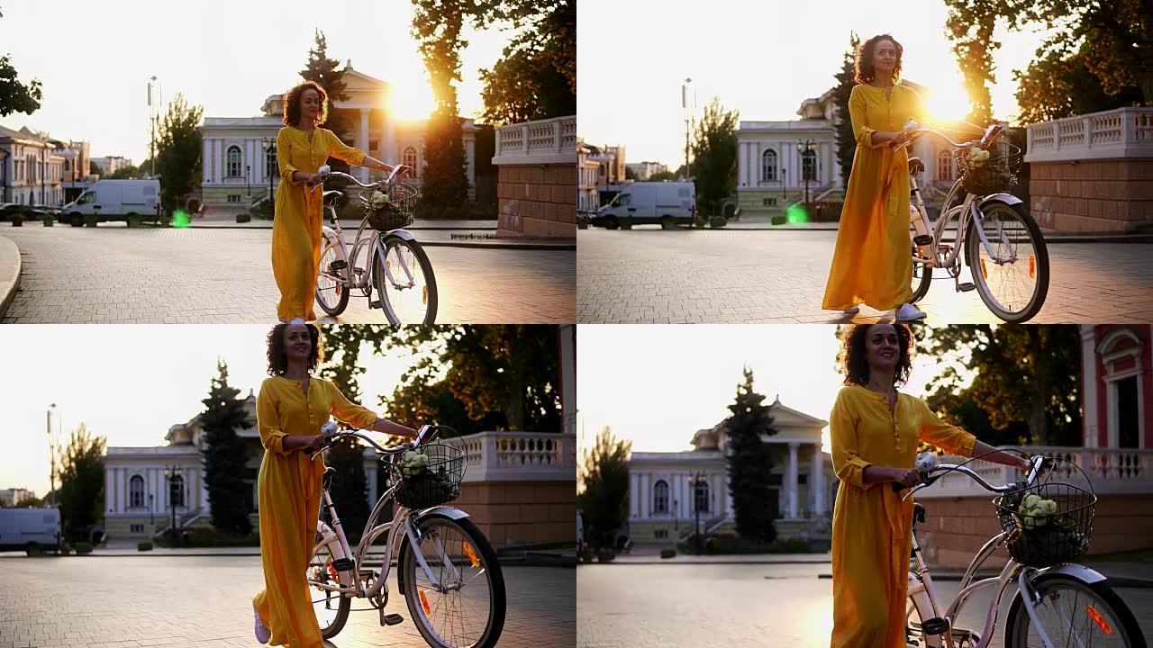 穿着黄色长裙微笑的黑发女人在黎明时拿着城市自行车的车把，篮子里放着鲜花。镜头耀斑，美丽的城市景观