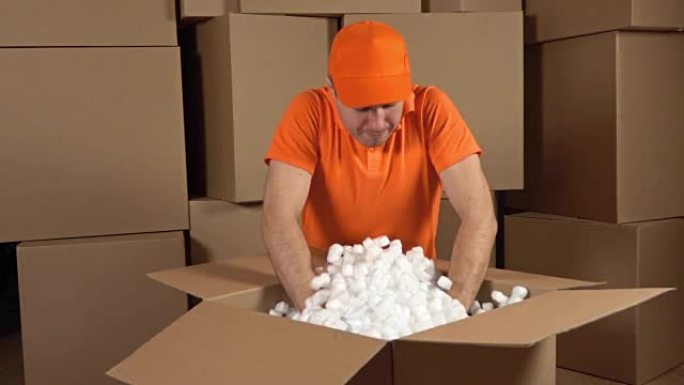 穿着橙色制服的仓库工人打开装满软包装材料的大纸箱。防震容器。多个盒子背景。慢动作视频