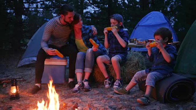 在大自然中靠近火焰的食物，家人在吃盐的玉米，在户外野餐，旅行露营，妈妈，爸爸和儿子吃光了