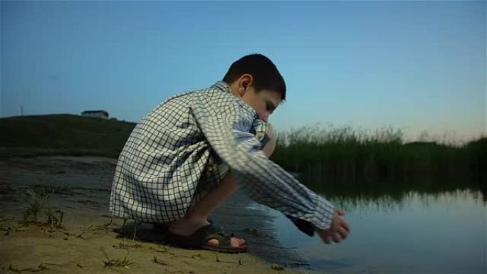 孤独的男孩在日落时从河底收集沙子