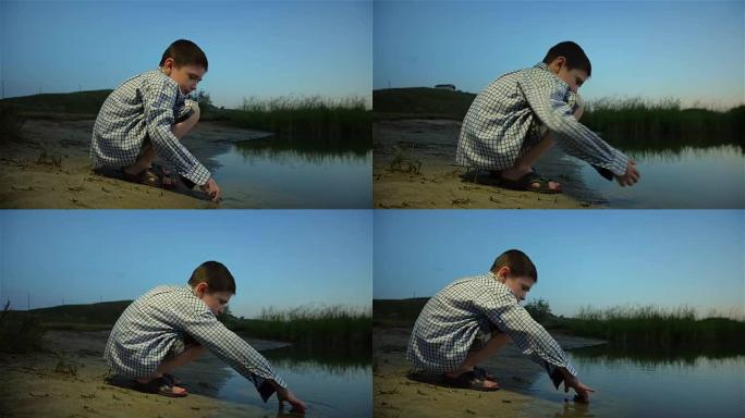 孤独的男孩在日落时从河底收集沙子