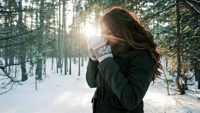 浪漫的女孩在背光的阳光下喝一杯，年轻的女人在冬天的森林里喝茶，咖啡