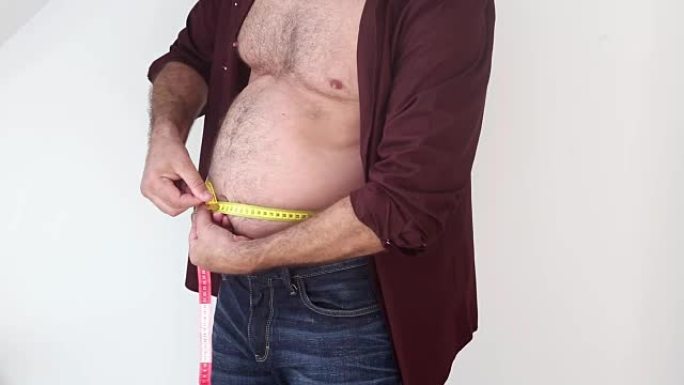 男人的特写测量他的胖肚子，并试图看起来瘦