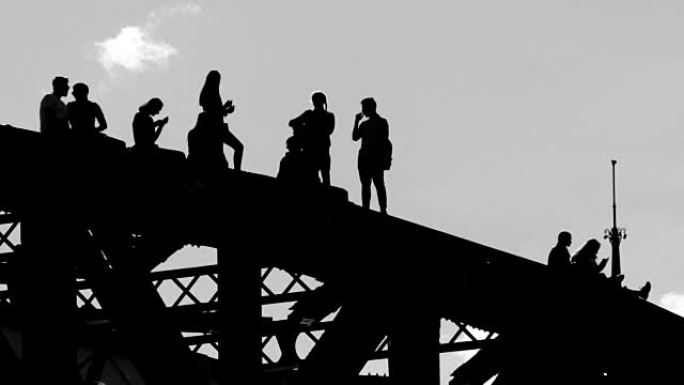 年轻人在桥顶上不稳定的情况下漫步并互相拍照的剪影