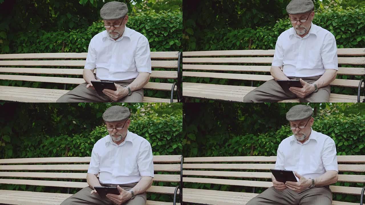 迷人的高级男子使用平板电脑，坐在公园FullHD的长凳上