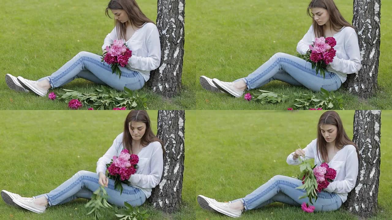 女人让牡丹花束坐在公园的草地上