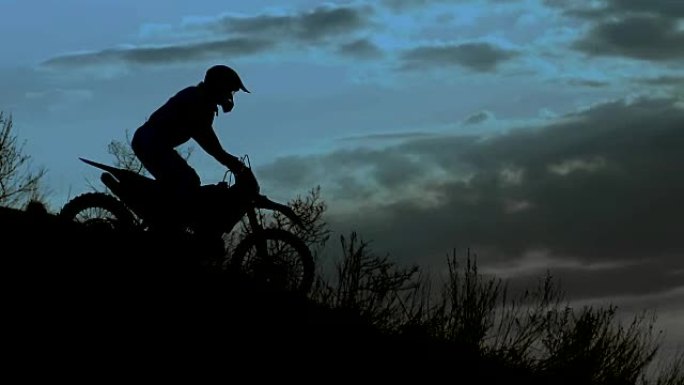 骑士在夜晚的剪影。他骑着极限摩托车下山