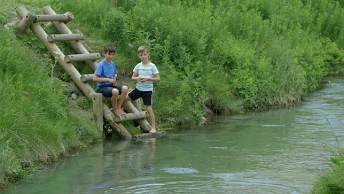两个小男孩玩得开心，把石头扔进河里。