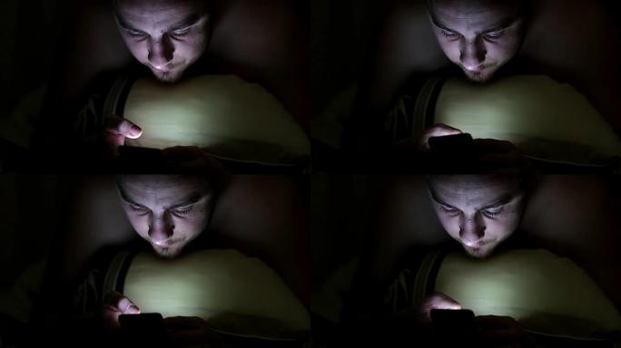 年轻人晚上在毯子下的床上使用智能手机