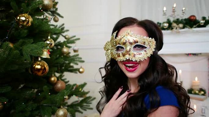 戴着面具庆祝新年的美丽女孩，圣诞节化妆舞会，圣诞树附近的派对，一个穿着漂亮晚礼服的年轻女子