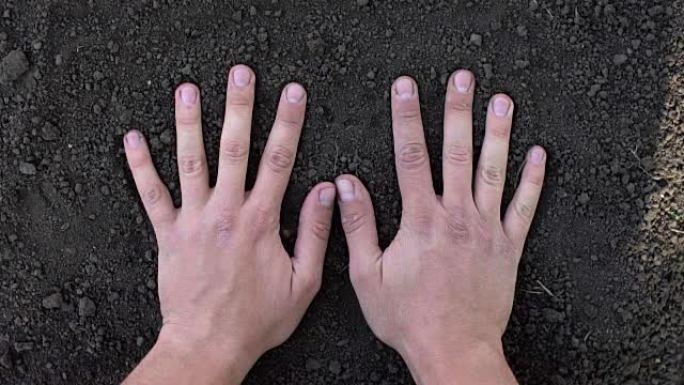 在黑土地上制作手印的人的手的特写