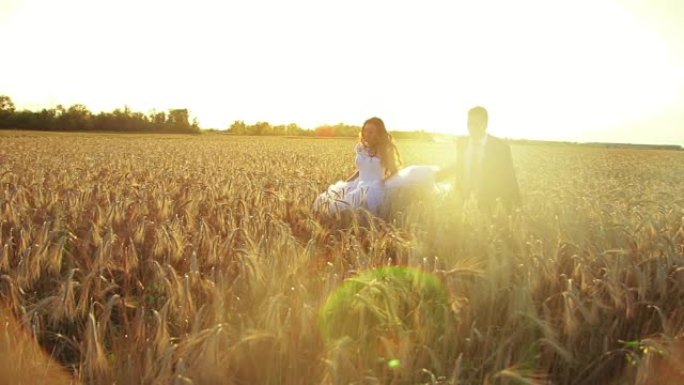 年轻美丽的夫妇新娘和新郎牵手在日落的麦田上奔跑，浪漫而温柔
