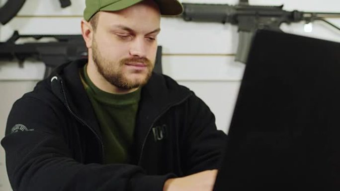 一个年轻人正在用一台笔记本电脑工作，接下来是一把枪
