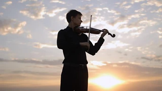 小提琴手在日落时在屋顶上演奏。音乐，艺术