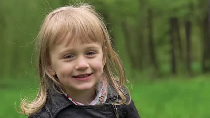可爱的金发小女孩在公园里微笑。慢慢地