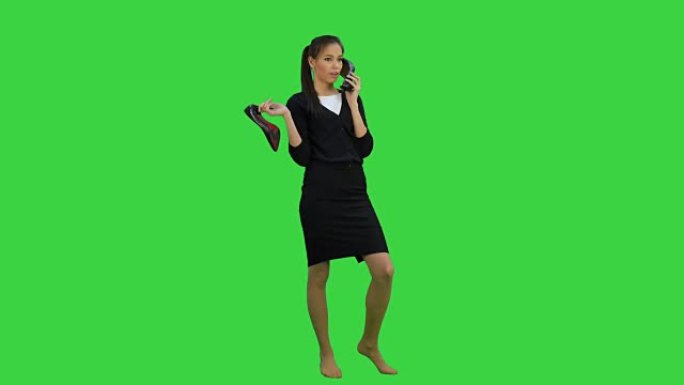 年轻的健谈女人在绿屏上使用像电话一样的鞋子，色度键