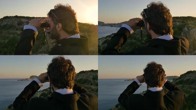 穿着优雅西装的男人，用公文包在岛上的悬崖顶上透过双筒望远镜看