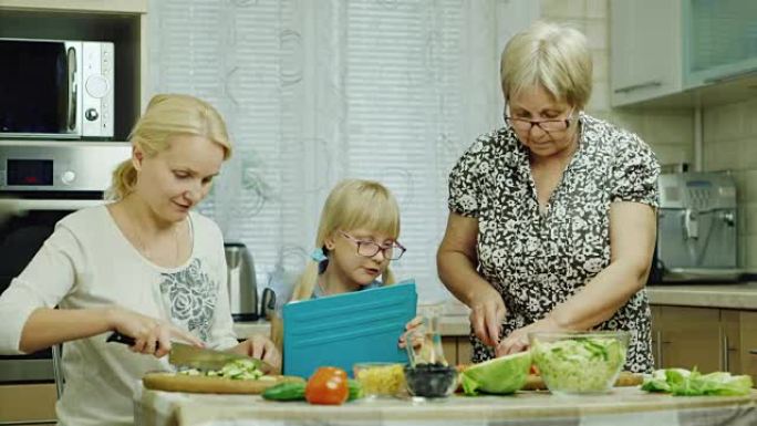 三代人，一家人一起在厨房里准备沙拉。奶奶、妈妈和孙女一起工作，用平板电脑