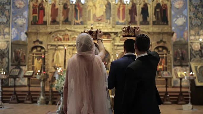 在法国尼斯东正教教堂圣像祭坛前的婚礼上，伴娘和伴郎站在新娘和新郎身后，手里拿着皇冠。