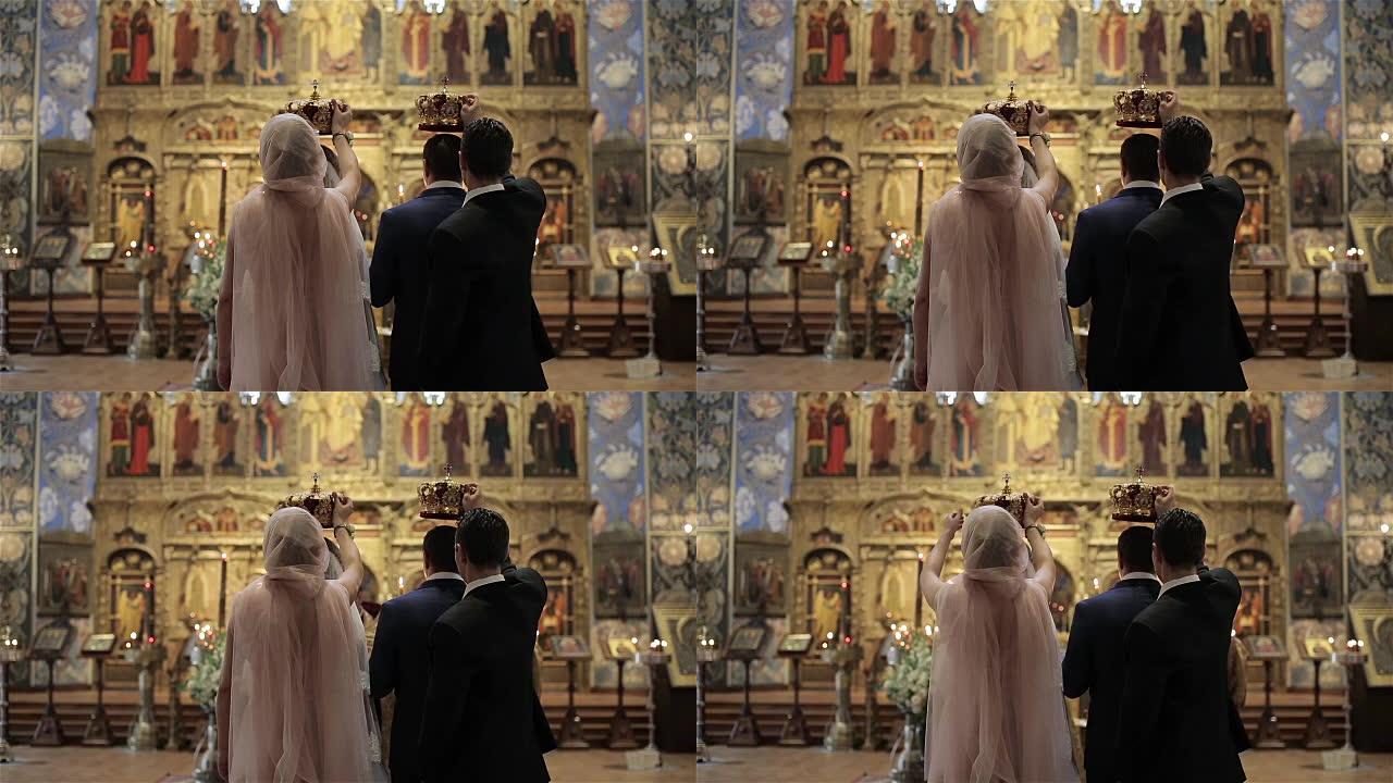 在法国尼斯东正教教堂圣像祭坛前的婚礼上，伴娘和伴郎站在新娘和新郎身后，手里拿着皇冠。