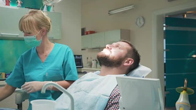 女牙医钻男性患者的牙齿，看着镜头。滑块镜头