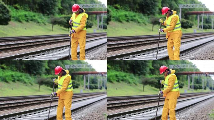身穿黄制服，手拿撬棍的铁路工人正在修理铁轨