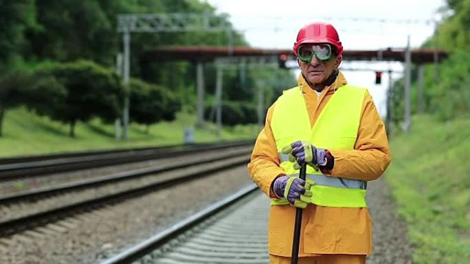 身穿黄色制服、手拿撬棍的铁路工人站在铁路线附近