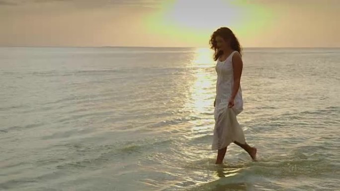 一位穿着淡淡的夏装的年轻女子在大海和日落的背景下沿着水边行走。一个很棒的假期。10位慢动作视频