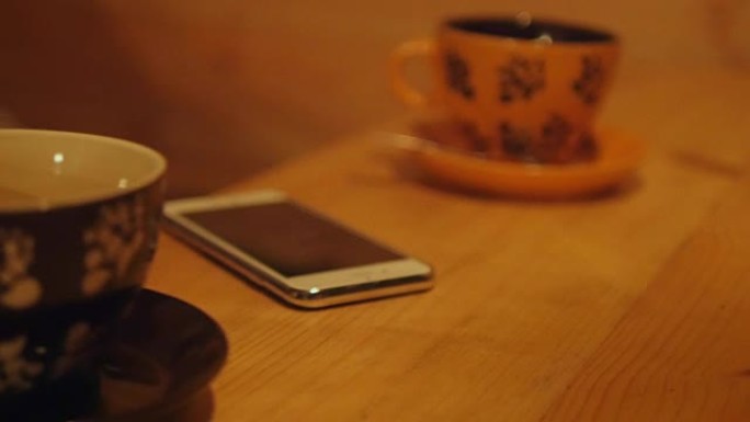 男人的手从木桌上拿手机。桌子上是一杯咖啡和电话。特写