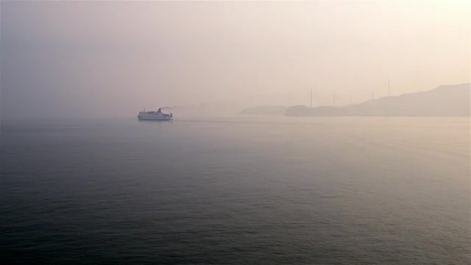 在雾蒙蒙的日子里，渡轮驶向韩国首尔仁川港，雾气中可见风力发电机的轮廓。