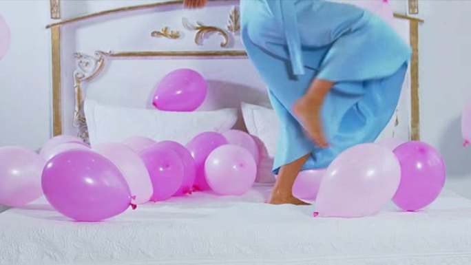 CU年轻女性踢气球在床上跳跃。60 FPS慢动作镜头