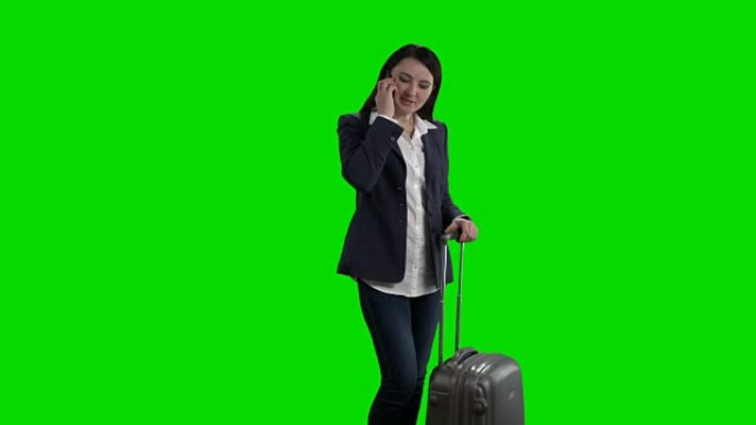 带着滚动手提箱的女人在绿屏上打电话