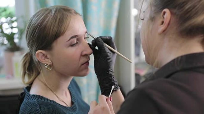 化妆师和模特。一个女人漂亮脸蛋的特写。化妆师在美容院的镜子前用专业刷子向漂亮女孩画眉毛。