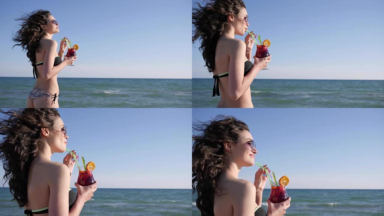 肖像微笑的女孩在海滩上，性感的女人与卷发饮料多彩的鸡尾酒，闪亮的海背景